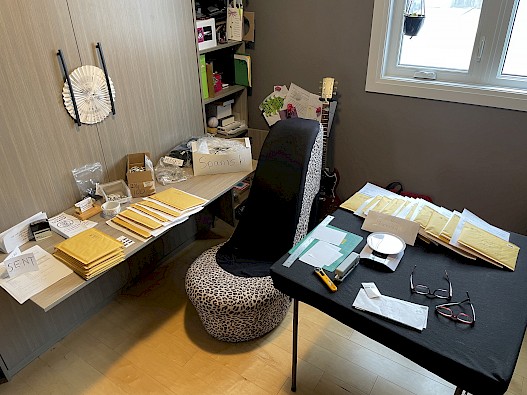 A small room with two tables covered with papers, padded envelopes, and boxes of checkered eyes.